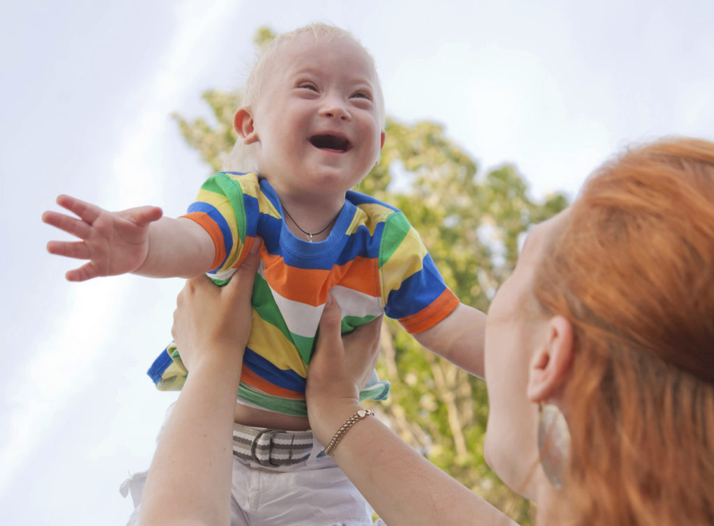 Baby with Down syndrome held in the air by her mother.