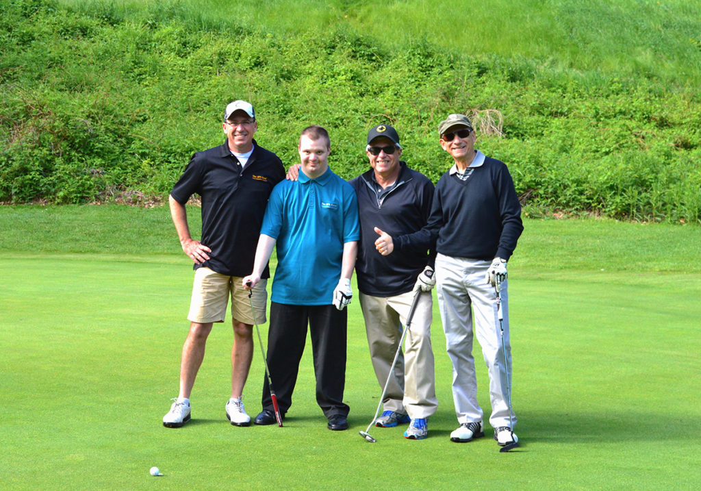 Four men, including one with Down syndrome, playing golf together.