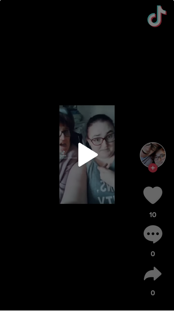 Image description of embedded TikTok video: Two women are seated side by side. The person on the left is wearing a cozy mauve top which coordinates with their burgundy hair. The person on the right is wearing a grey tank top with hair pulled back in a casual ponytail. Both are smiling mischievously and wearing glasses. 